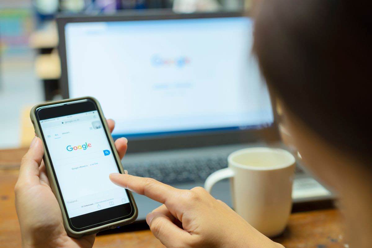 Persona con computer e smartphone in mano e pagina Google
