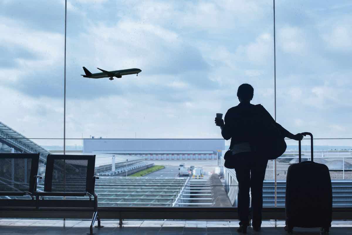 Persona in aeroporto con aereo in decollo sullo sfondo 